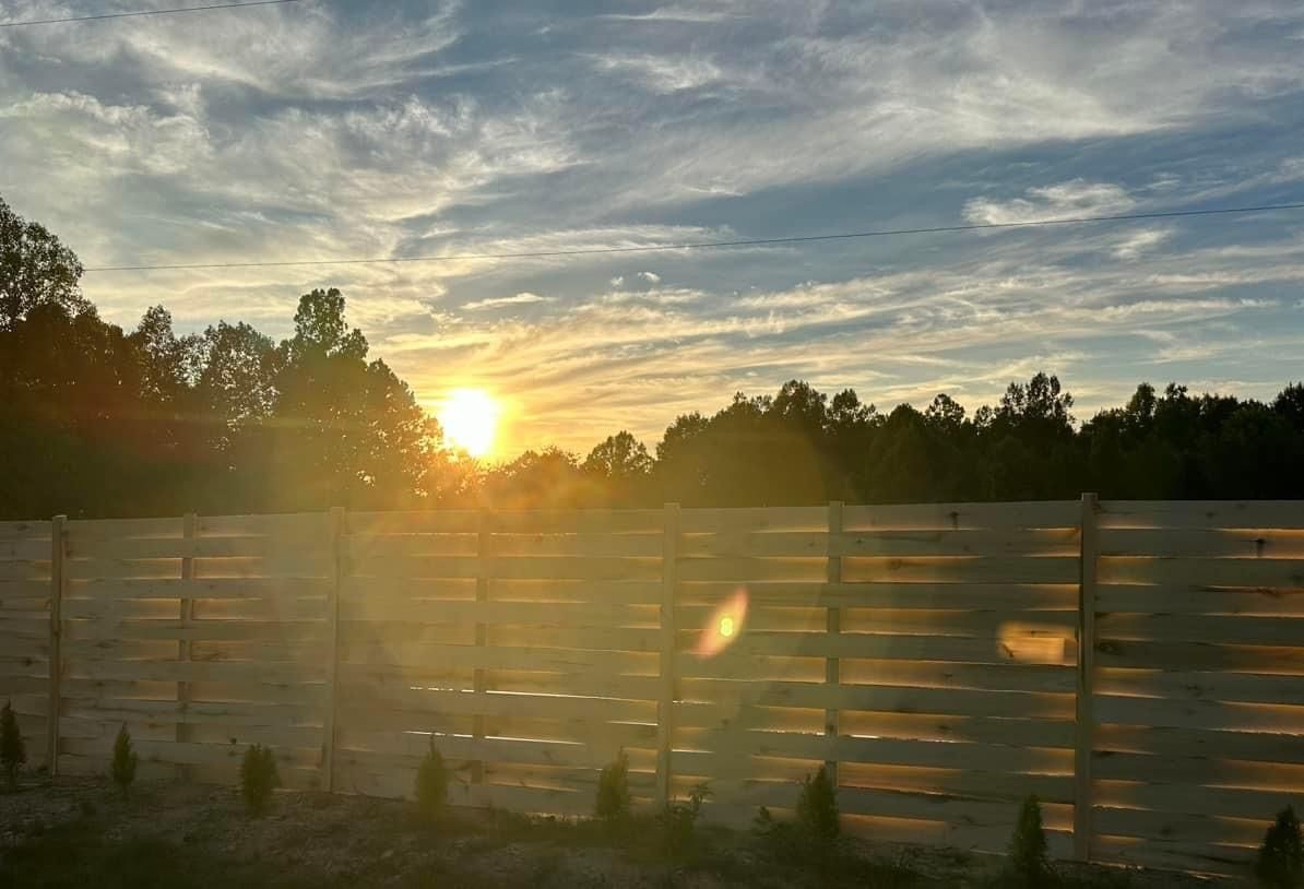 The sun is setting behind a wooden fence.