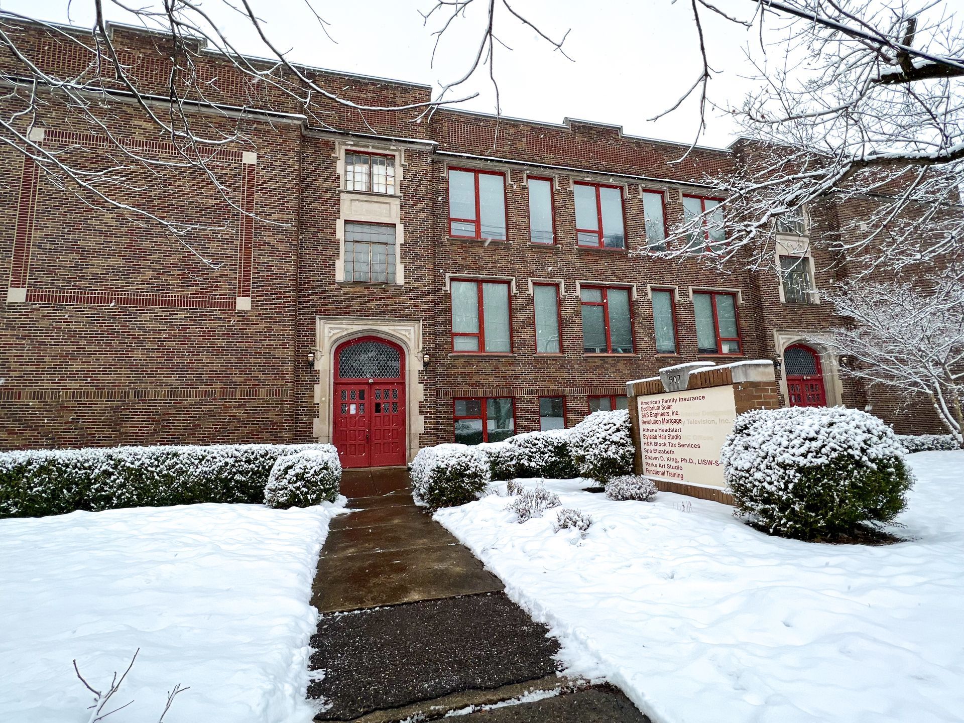 A large brick building with a red door is covered in snow.