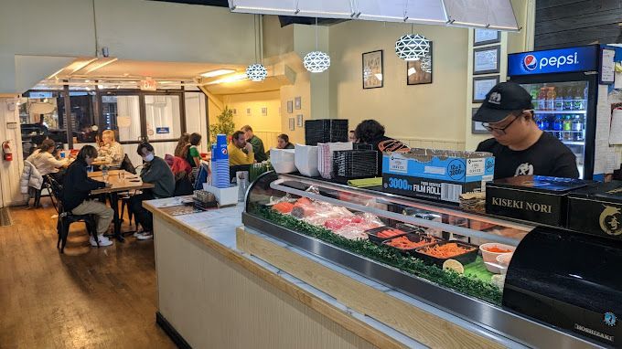 A man is standing behind a sushi counter in a restaurant.