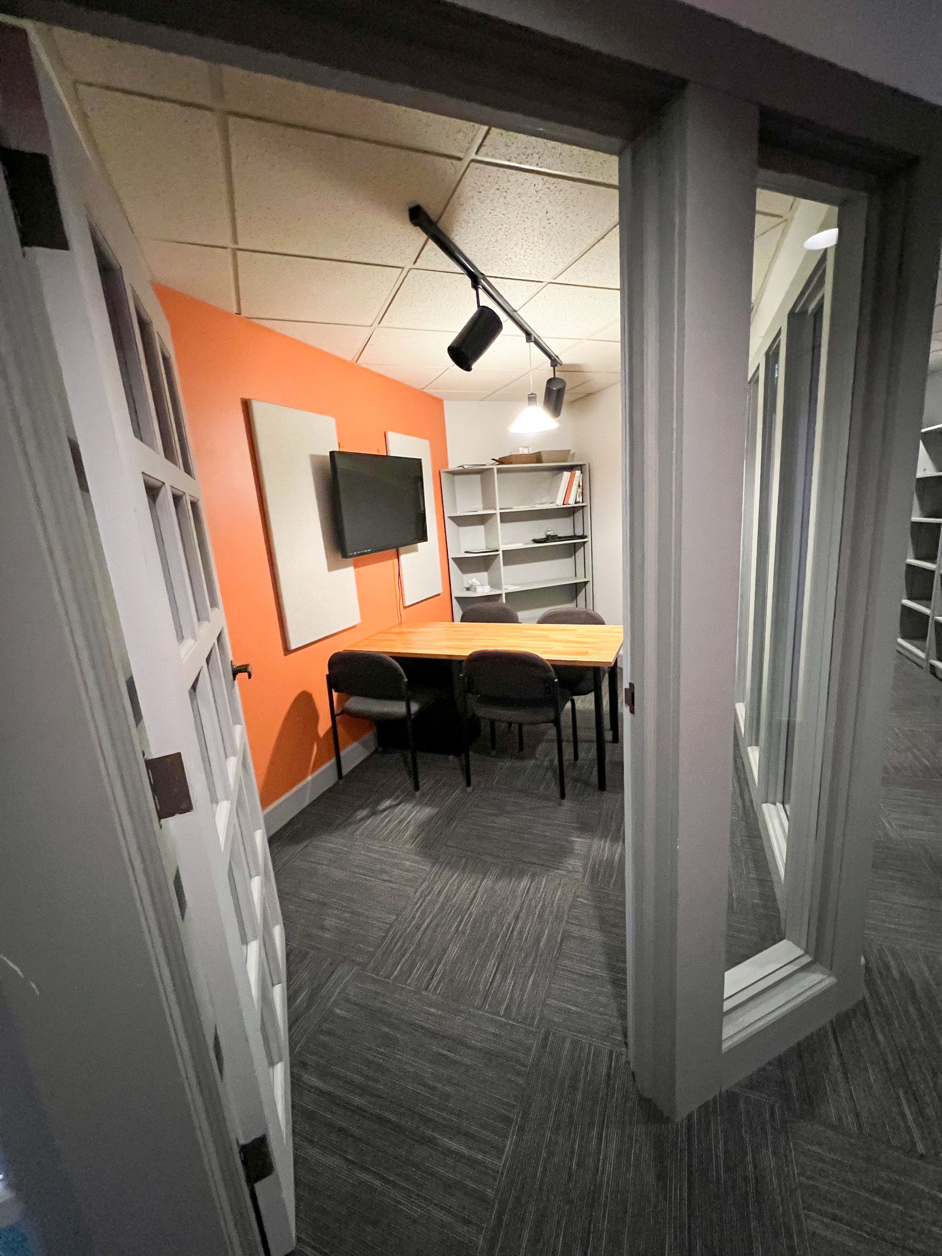 A conference room with a table and chairs and a television on the wall.