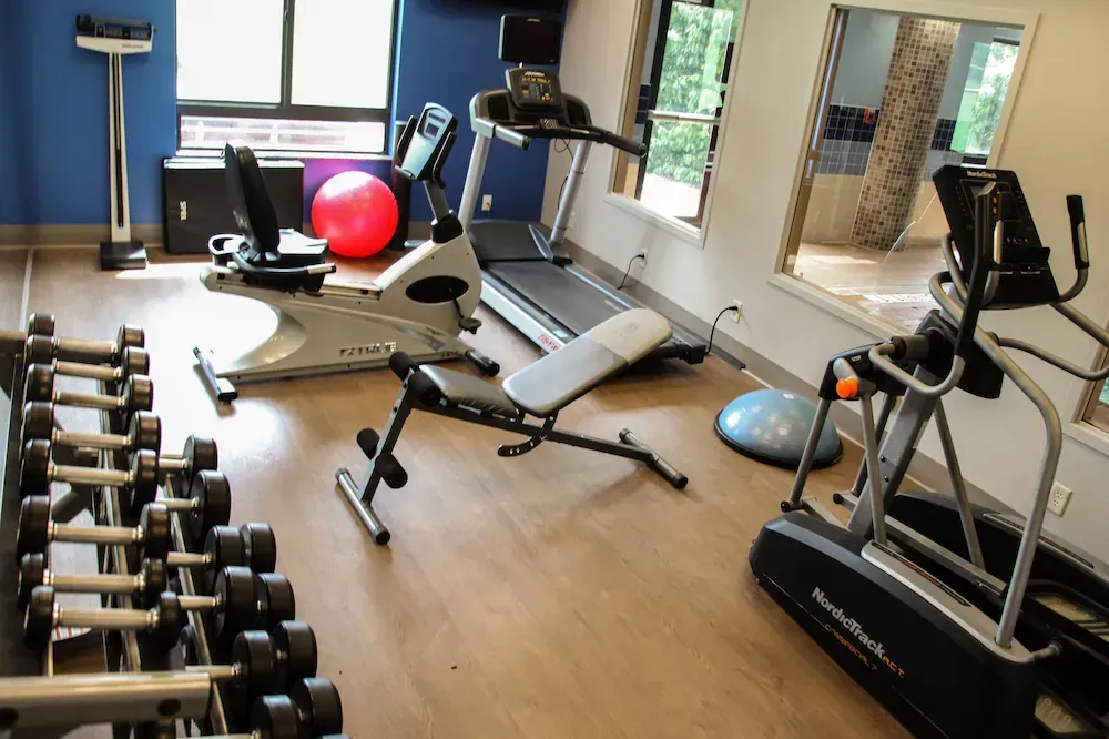 A gym with a treadmill , elliptical , dumbbells , and a bench.