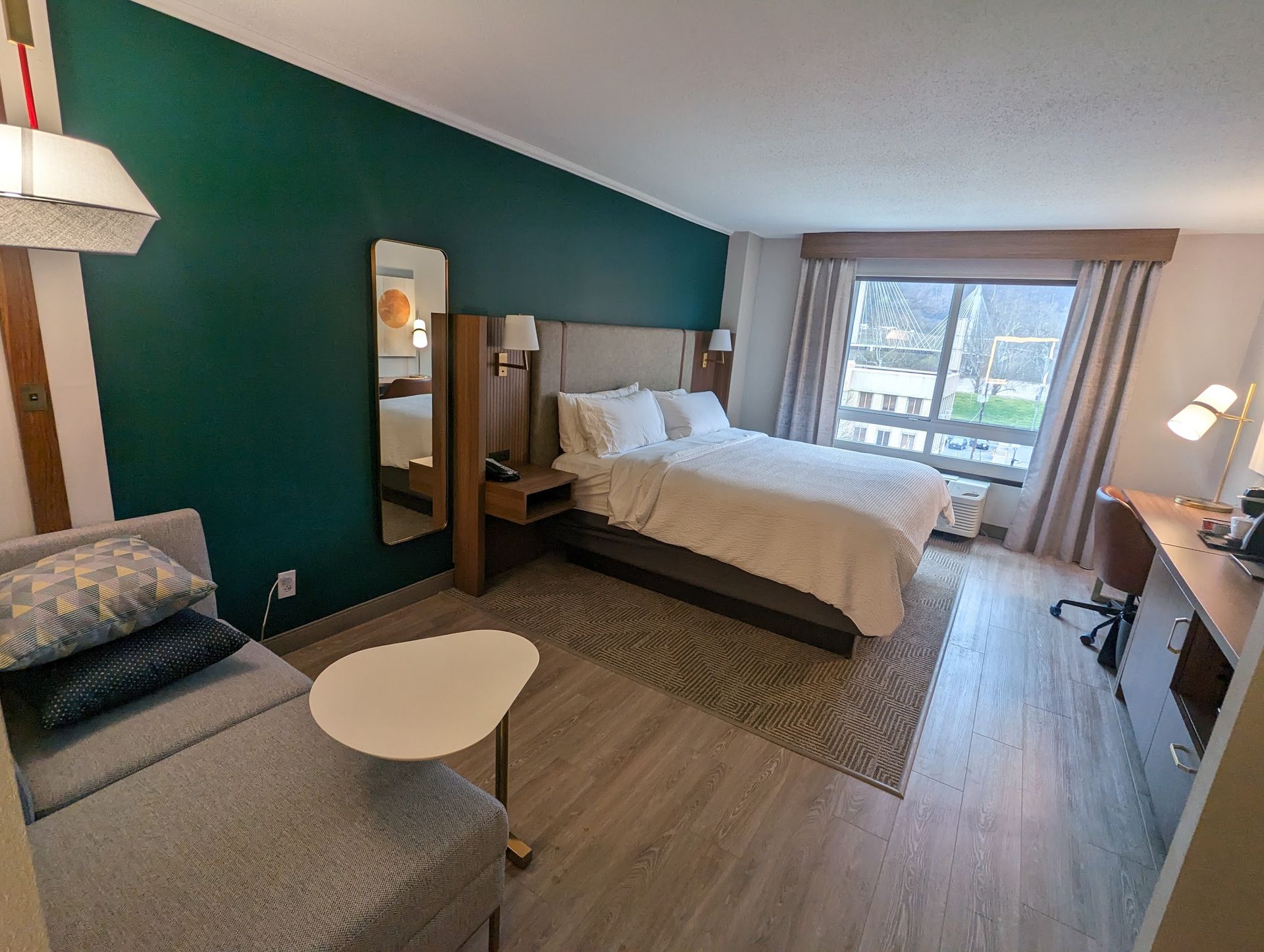 A hotel room with a king size bed , couch , desk and mirror.