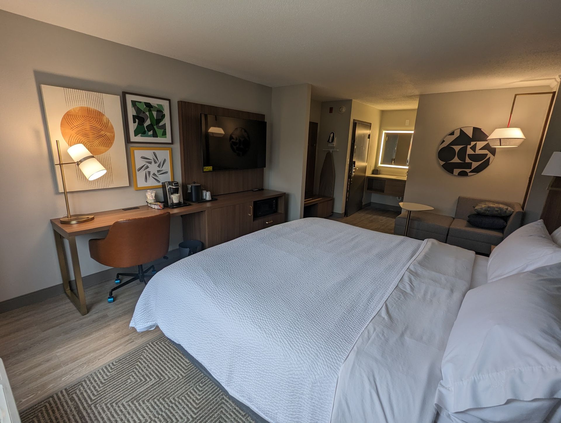A hotel room with a king size bed , desk , chair and television.