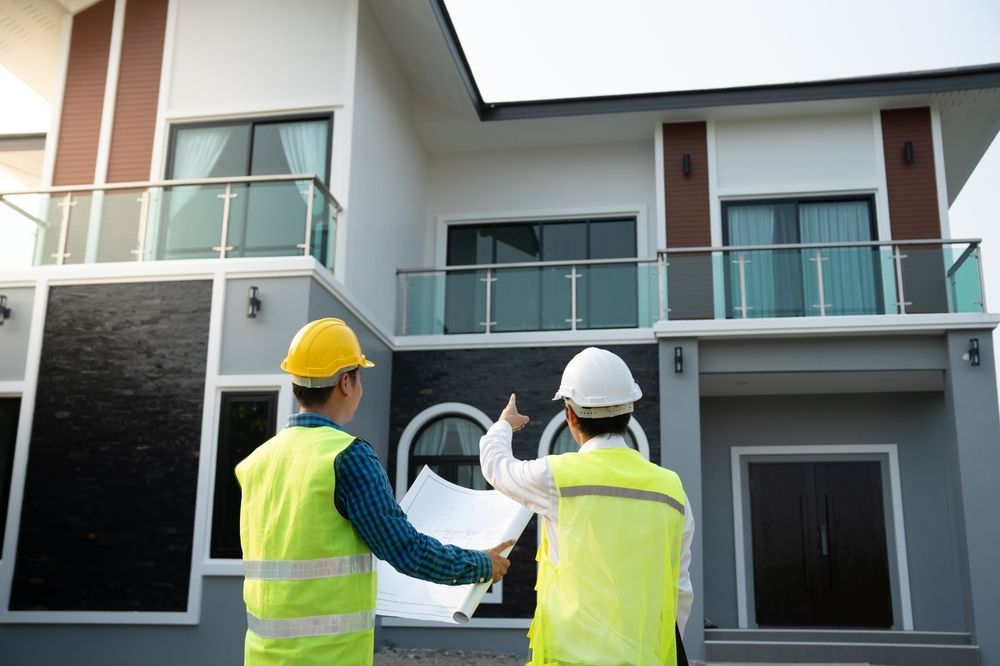 Two construction workers are looking at a blueprint in front of a house.