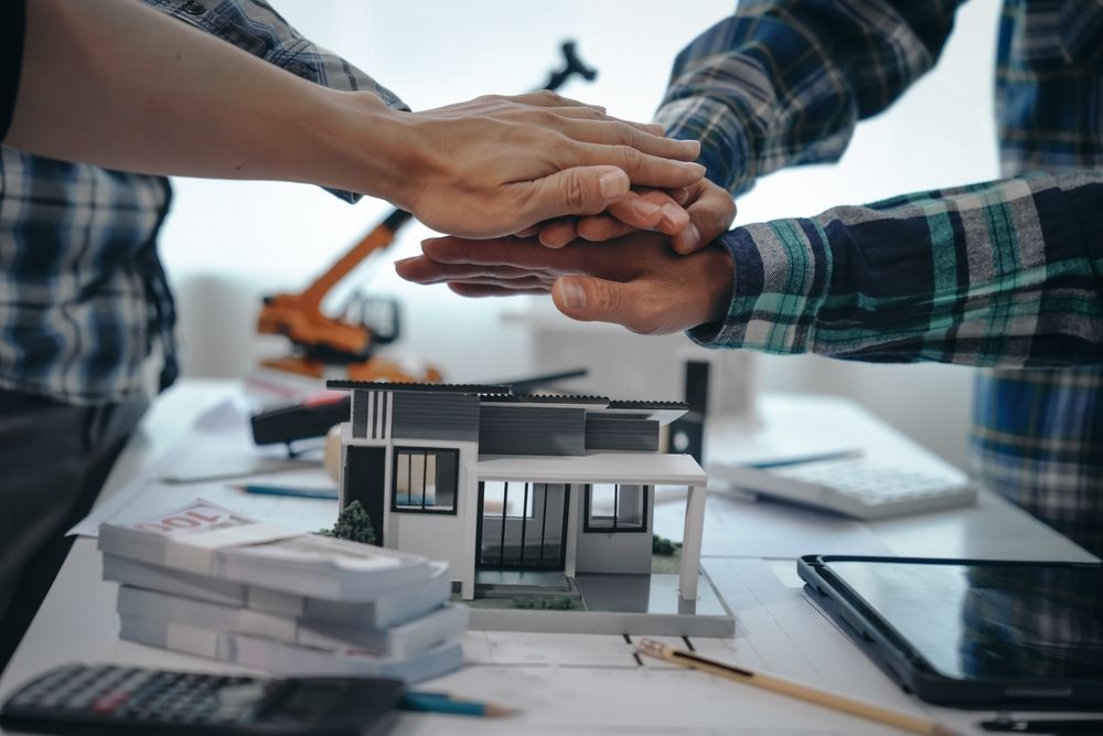 A group of people are putting their hands together in front of a model house.