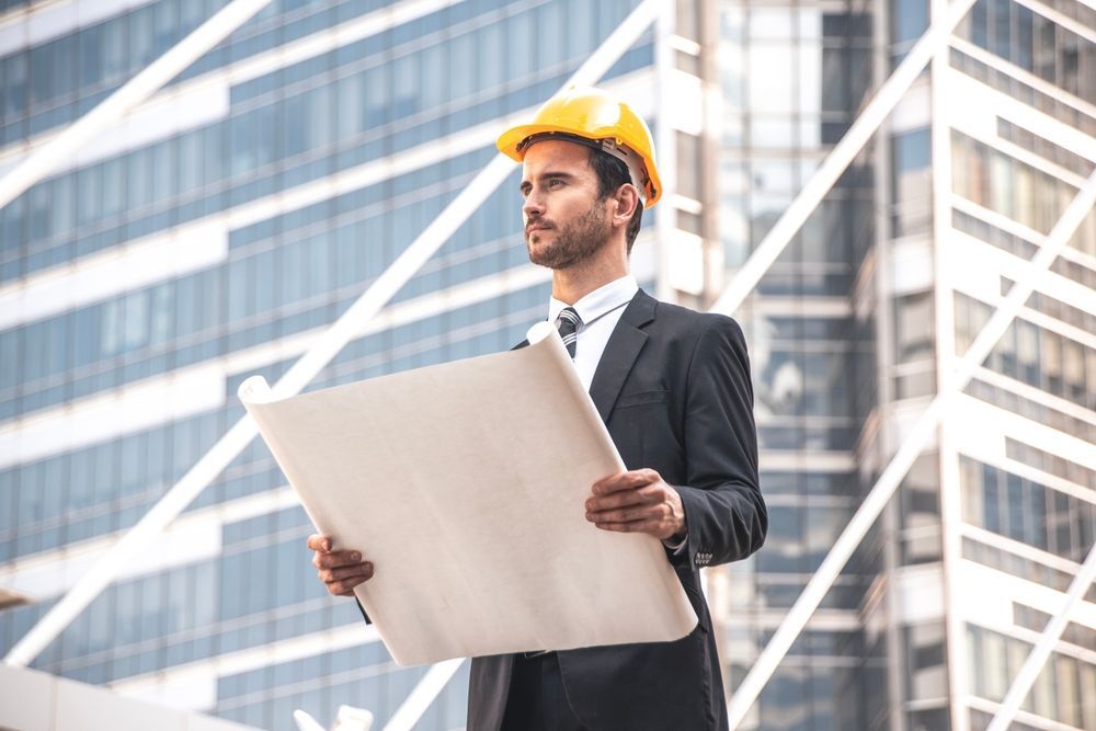 An architect in suit and helmet holding blueprints outdoors.