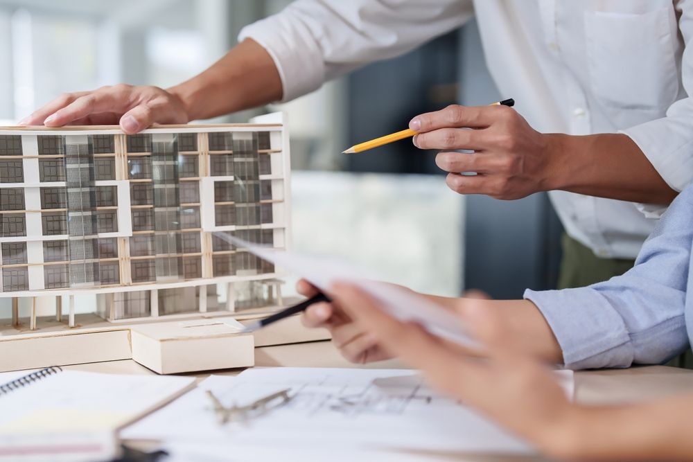 Two architect engineer inspecting building model and blueprint.