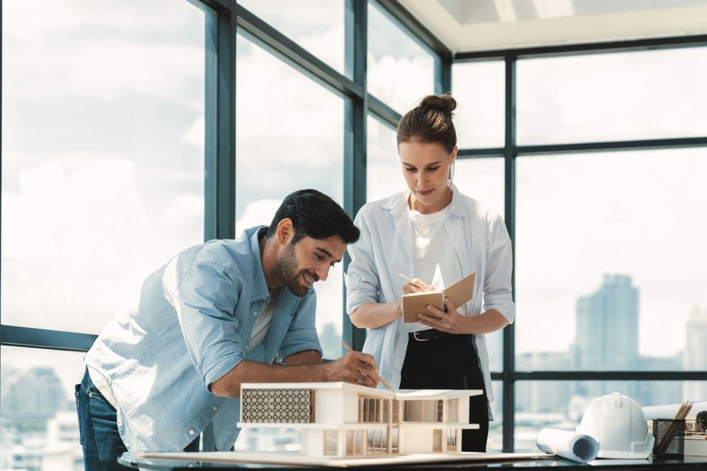 Two engineers are helping to design work on blueprints.