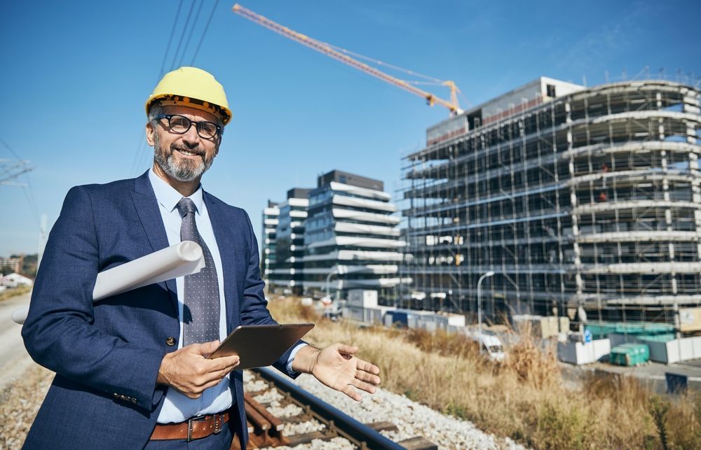 Senior architect wearing a protective helmet using a tablet and a blueprint on the construction site.