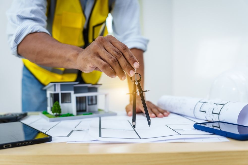 An architect is using a compass to draw a house on a blueprint.