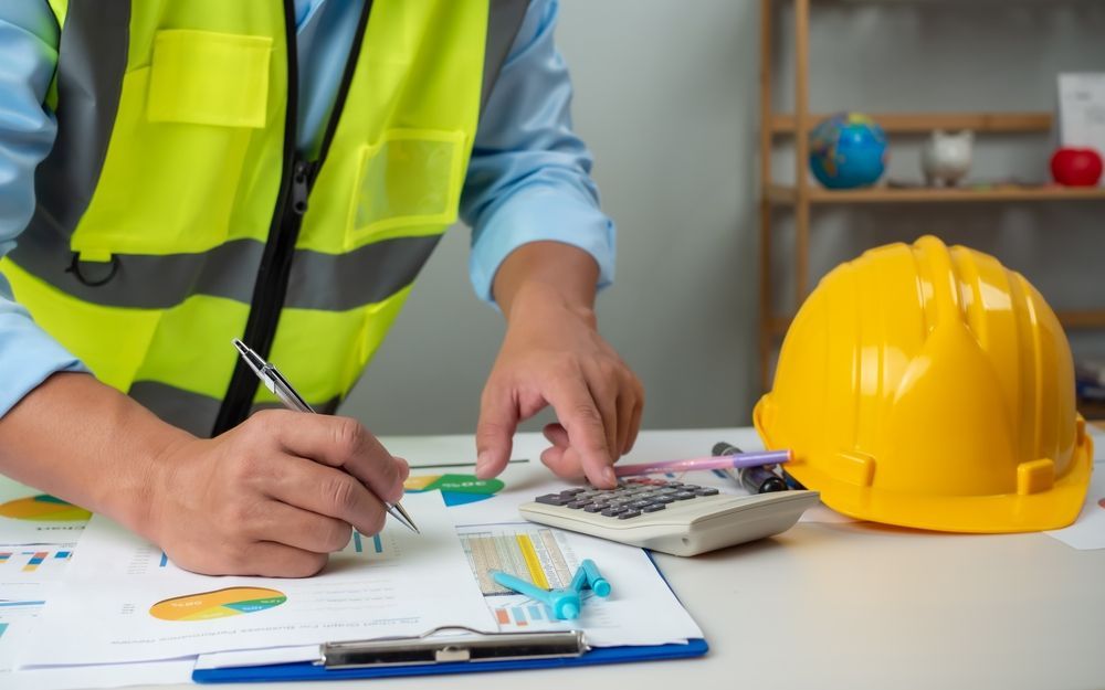 A construction worker is using a calculator and writing on a clipboard.