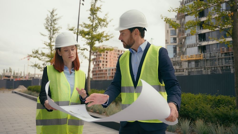 A man and a woman are looking at a blueprint on a construction site.