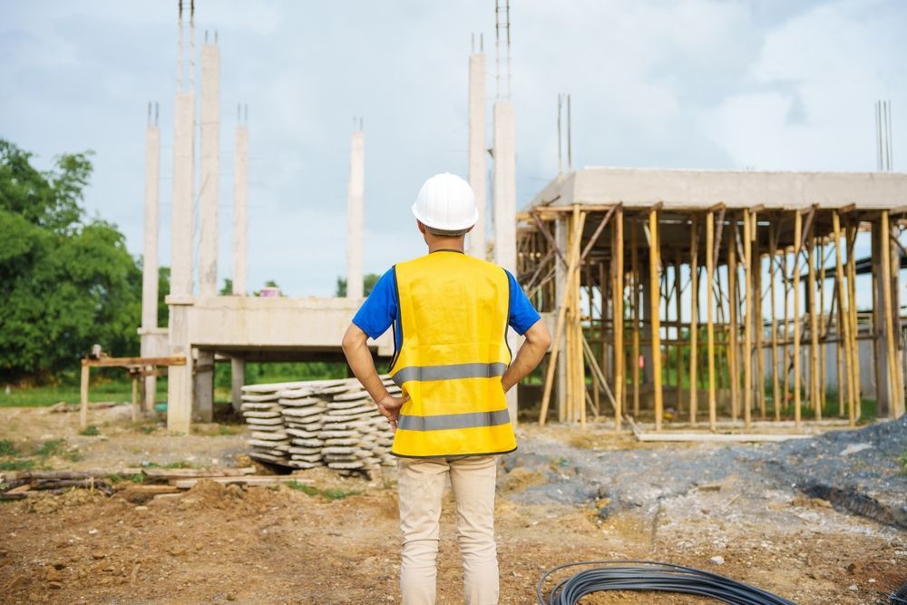 A construction worker is standing in front of a building under construction.