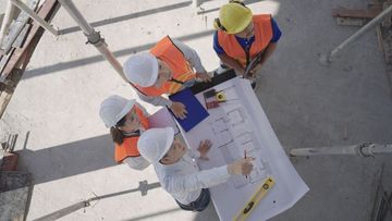 A group of construction workers are sitting around a table looking at a blueprint.