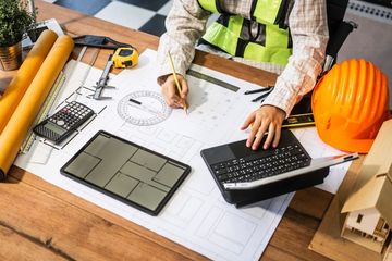 A construction worker is sitting at a table working on a blueprint.