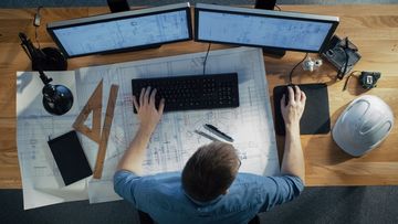 An architect is sitting at a desk working on a computer.