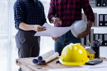 Two men are standing next to each other looking at a piece of paper.