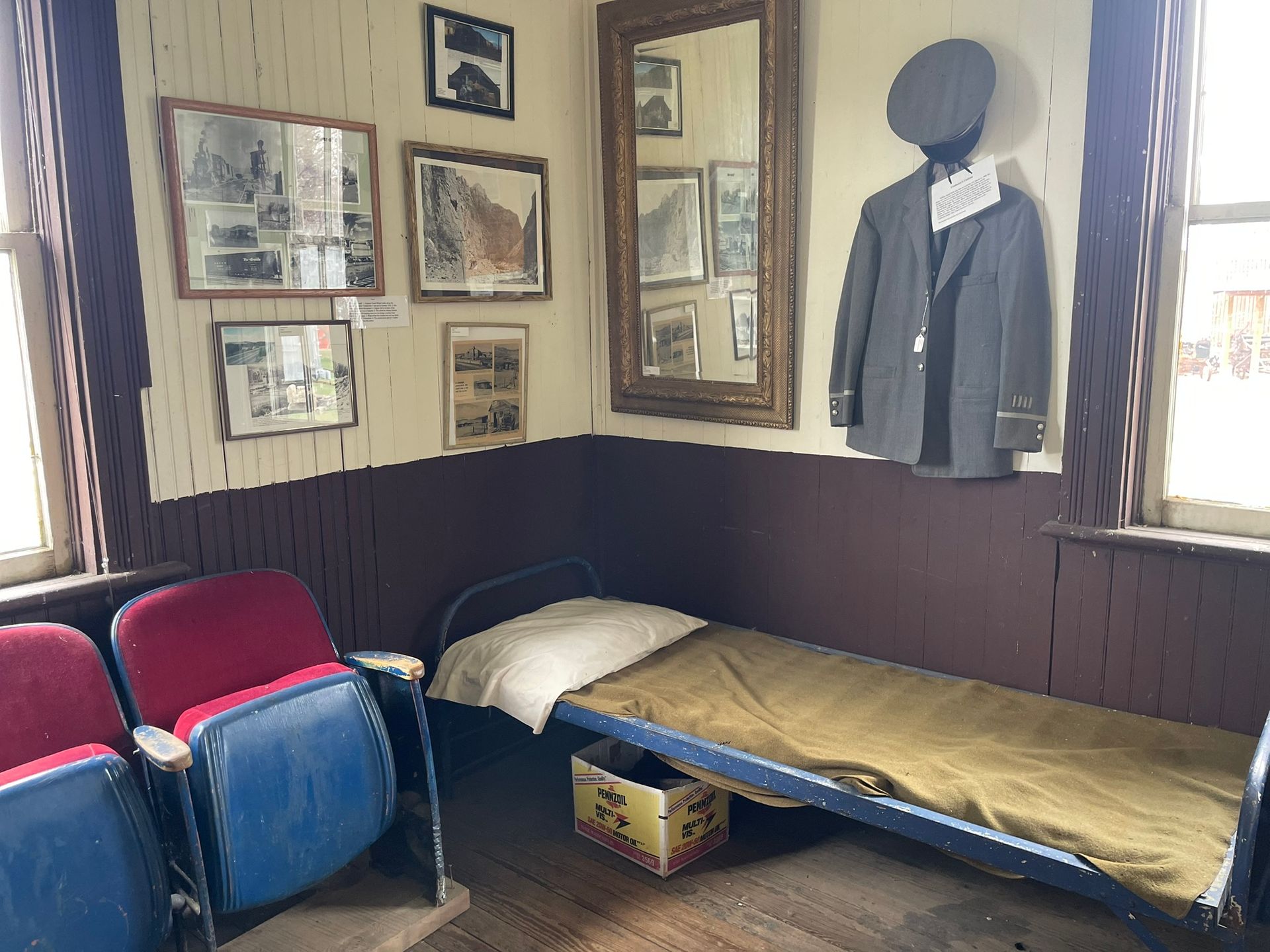 A room with a bed , chairs and a suit hanging on the wall.