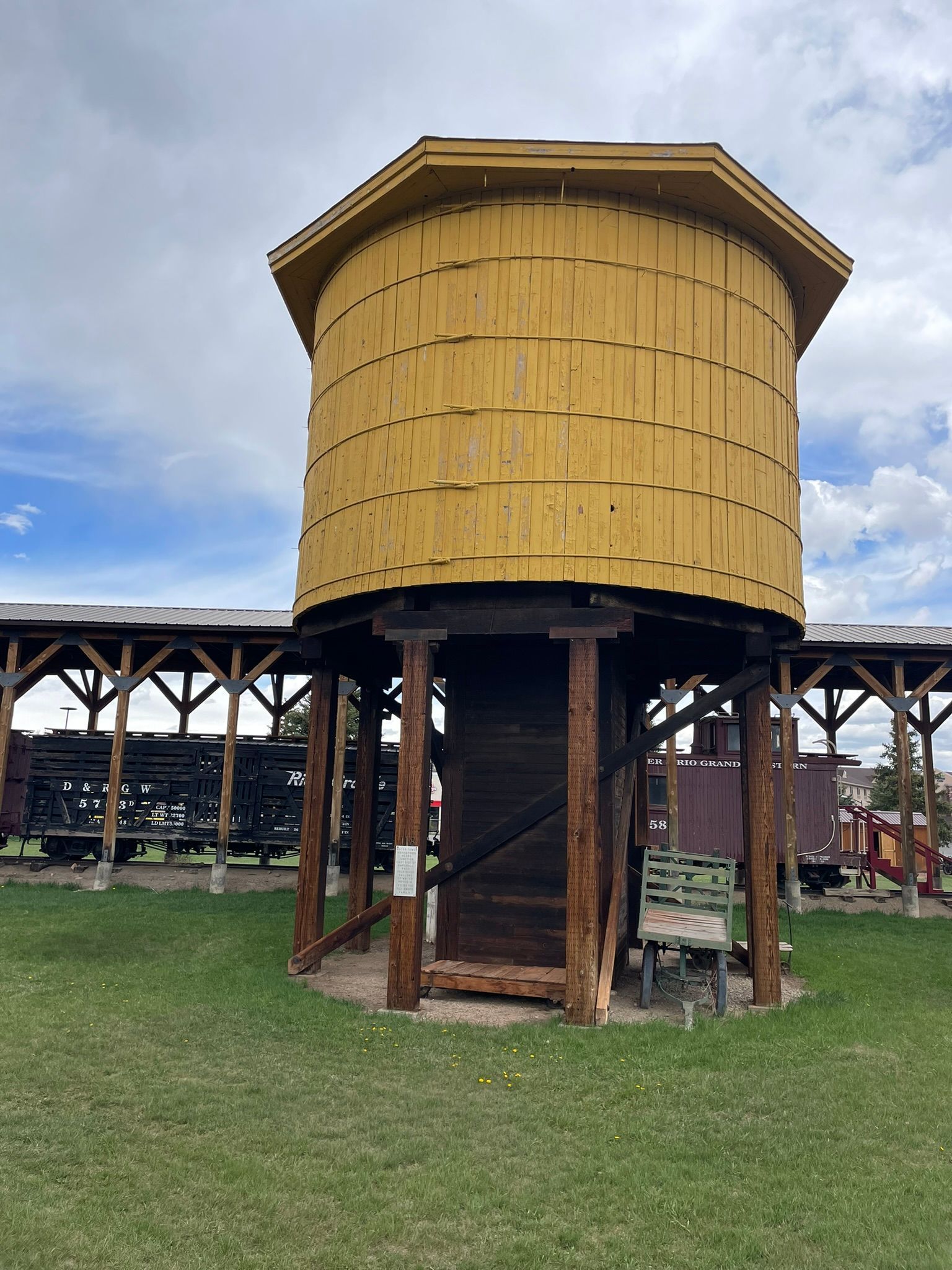 A large yellow water tower is sitting in the middle of a grassy field.
