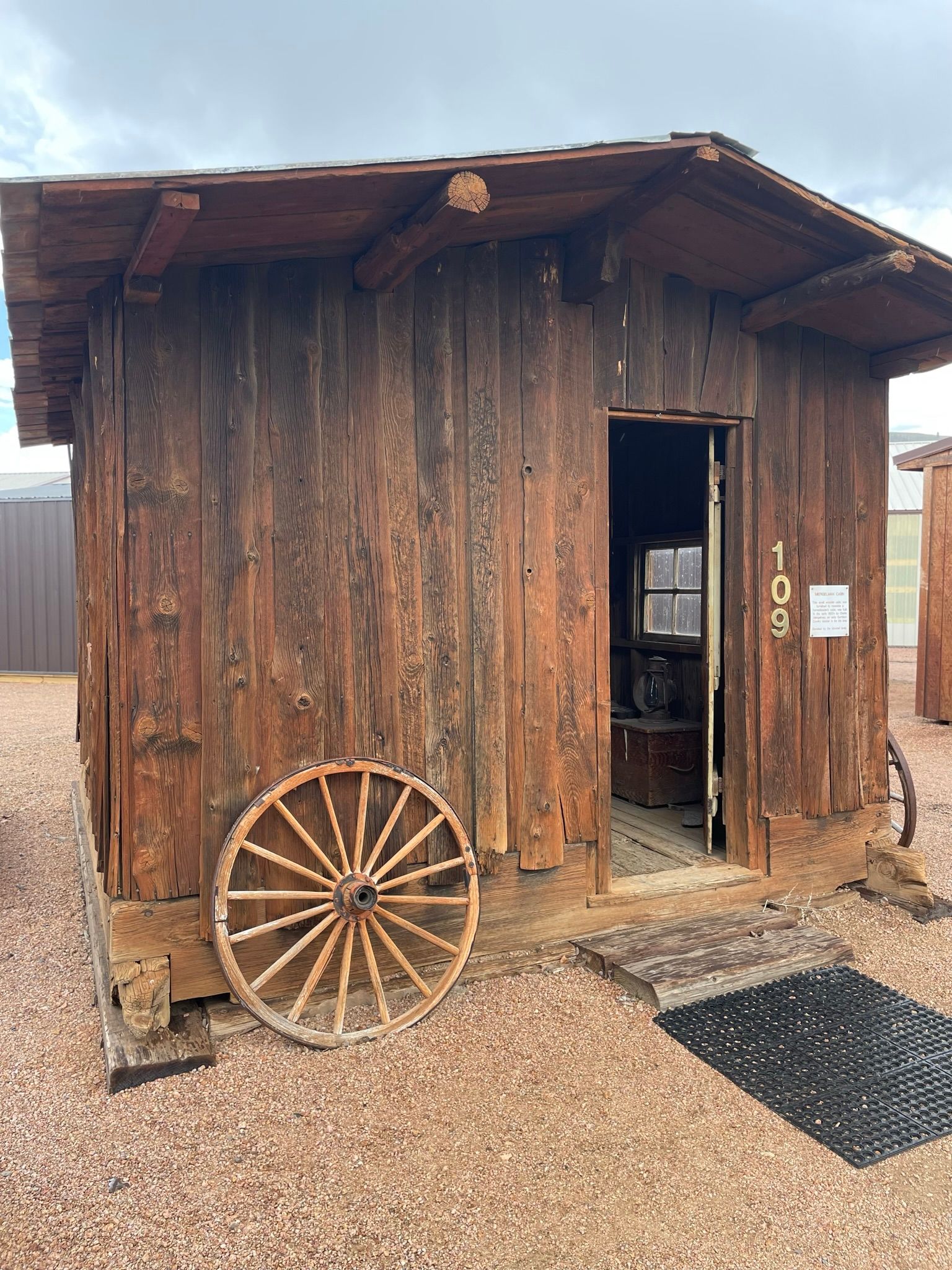 A wooden shed with a wagon wheel in front of it.