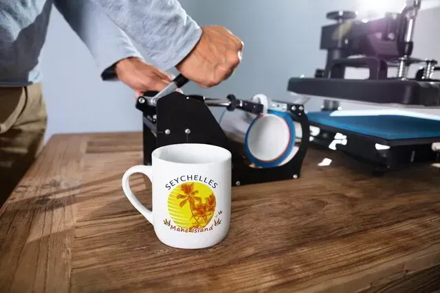 A person is printing a mug on a wooden table.