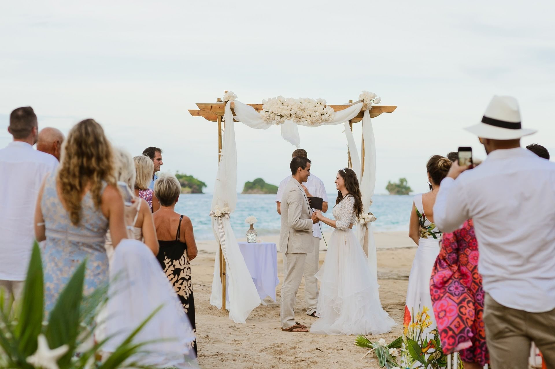 A man is taking a picture of a bride and groom during their wedding ceremony on the beach.