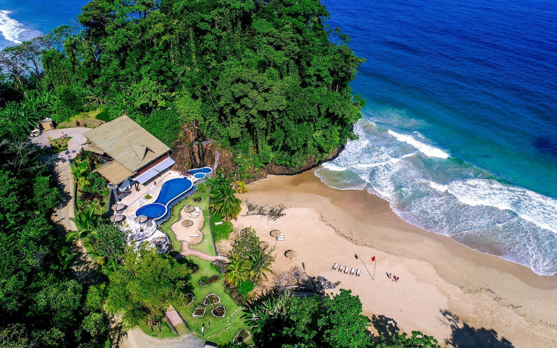 An aerial view of a beach with a house and a pool surrounded by trees.