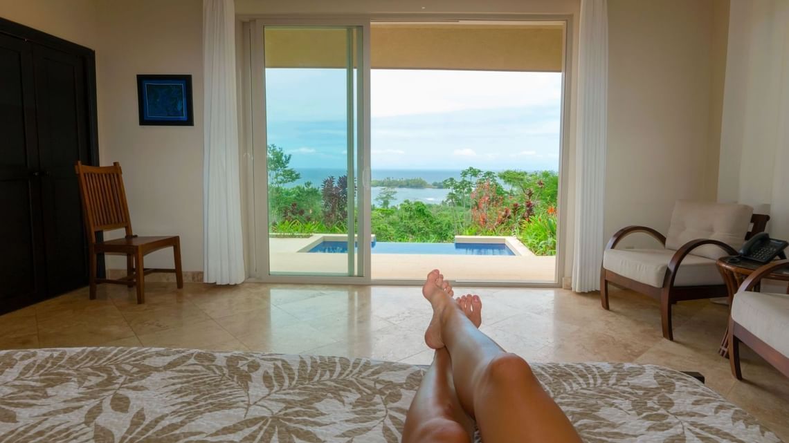 A woman is laying on a bed in a room with a view of the ocean.