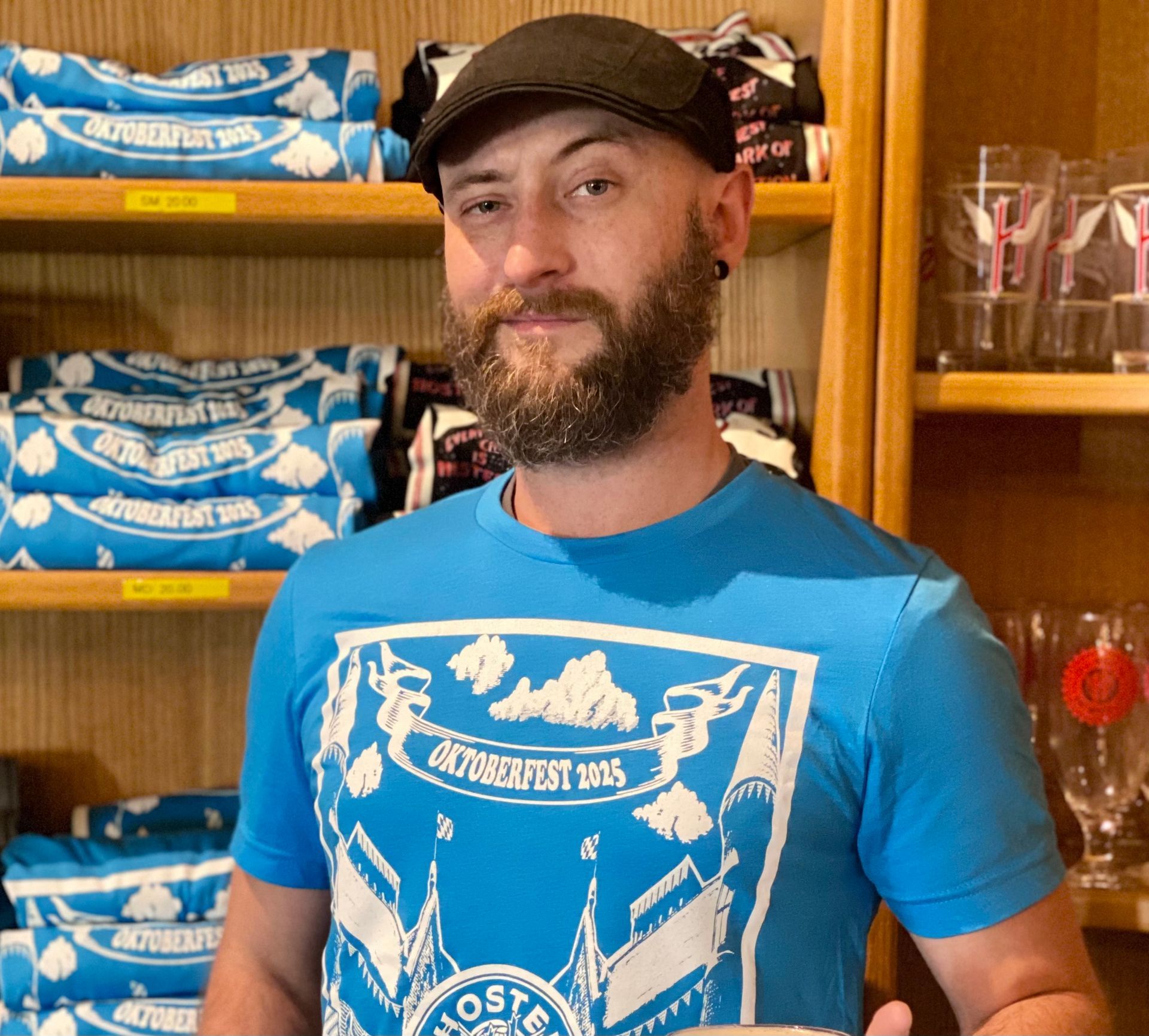 Ian Hansford, Taproom Manager wearing Hoster Oktoberfest t-shirt and holding a mug of beer