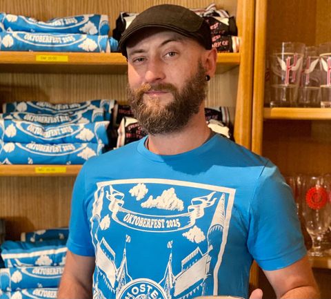 Ian Hansford, Taproom Manager wearing Hoster Oktoberfest t-shirt and holding a mug of beer
