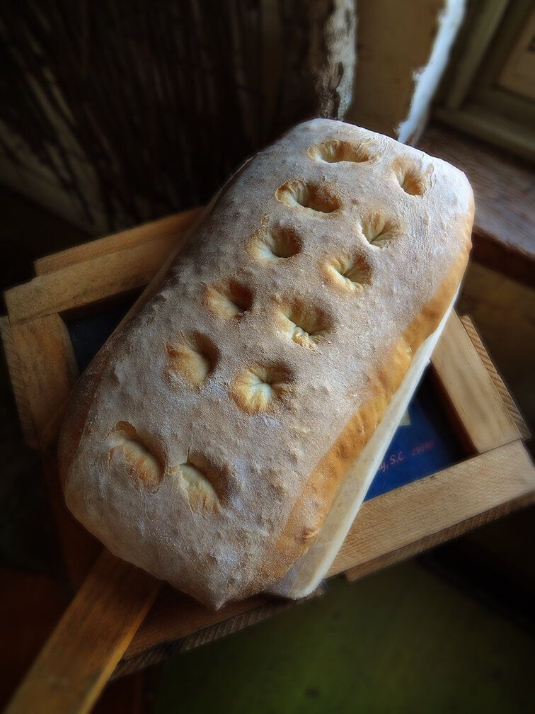 A loaf of focaccia bread with dimpled indentations on top, resting on a wooden board.