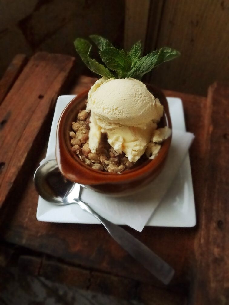 A scoop of vanilla ice cream topped with mint leaves, served in a ceramic bowl over a white square plate with a spoon.