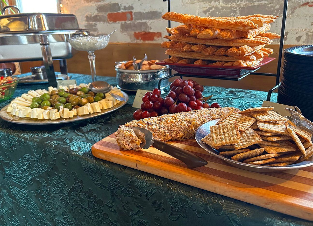 Appetizer buffet table with a cheese and olive platter, grapes, a nut-covered cheese log, crackers, and breadsticks.