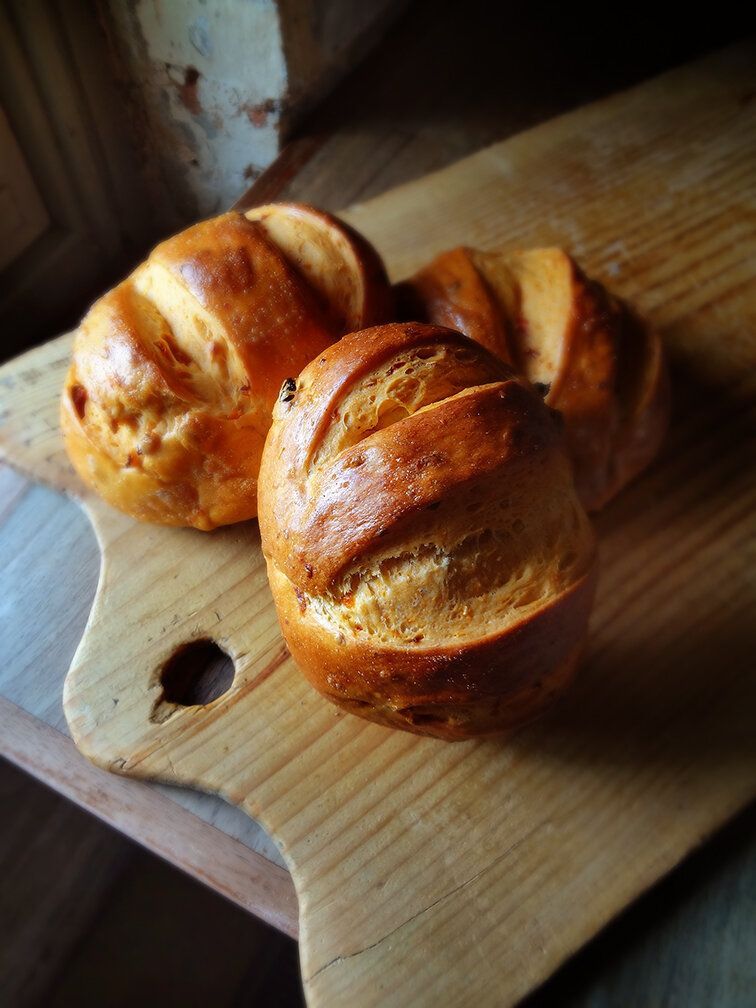 Three golden-brown, scored bread rolls resting on a wooden cutting board.
