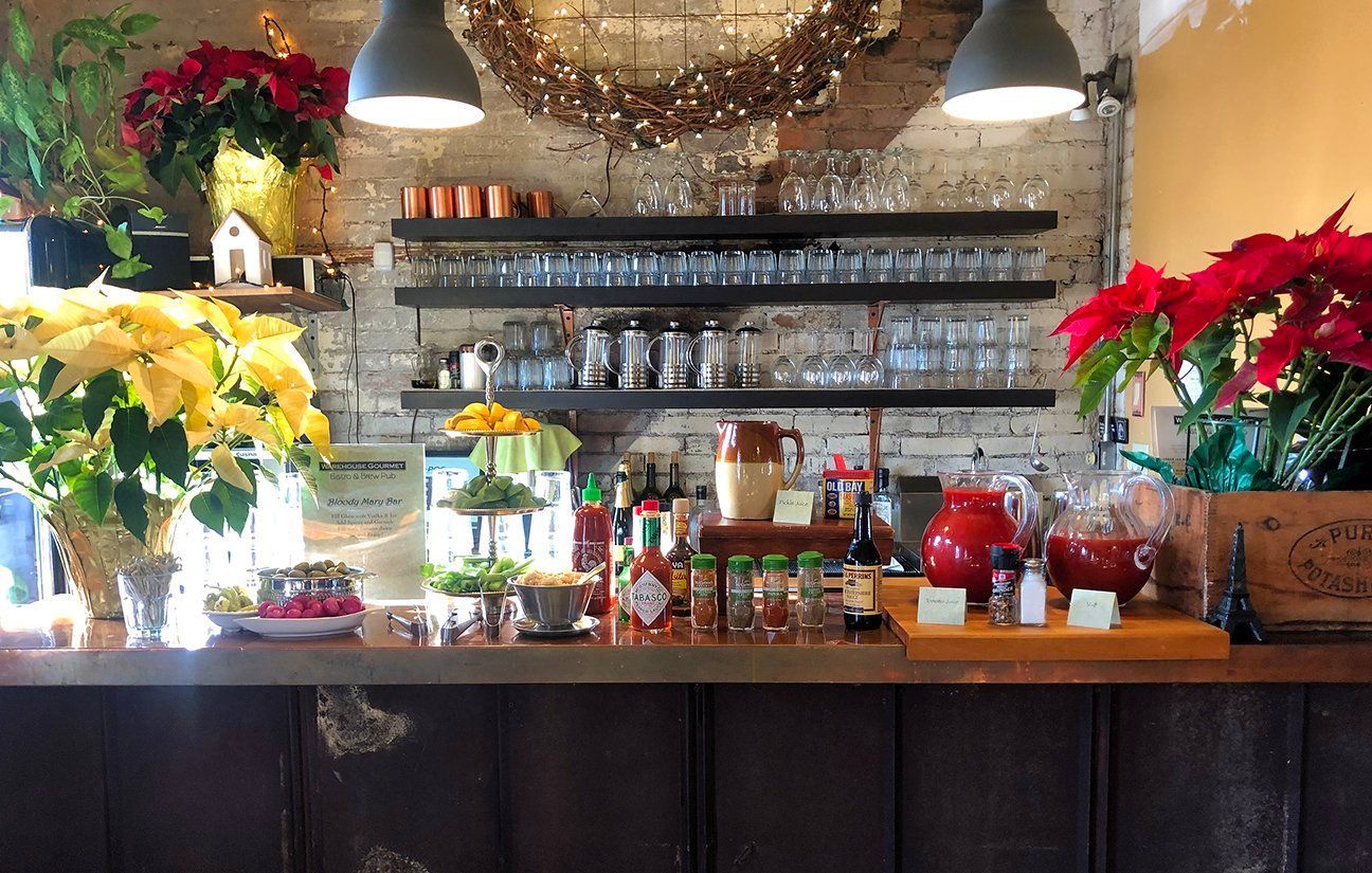 A wooden bar counter featuring two poinsettia plants, shelves of glassware, various condiments, and two hanging lamps.