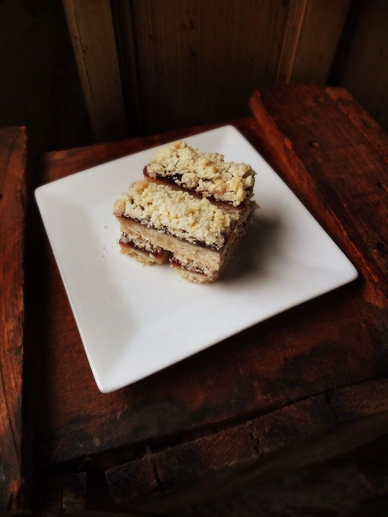Two stacked crumble bars with dark fruit filling, served on a square white plate set on a rustic wooden surface.