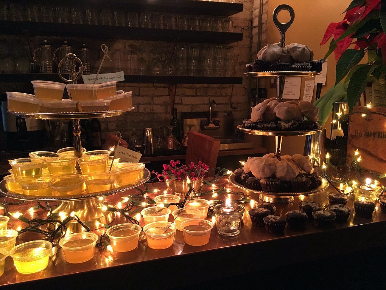 A dessert table set with tiered stands of pastries and individual jelly cups, illuminated by warm string lights.
