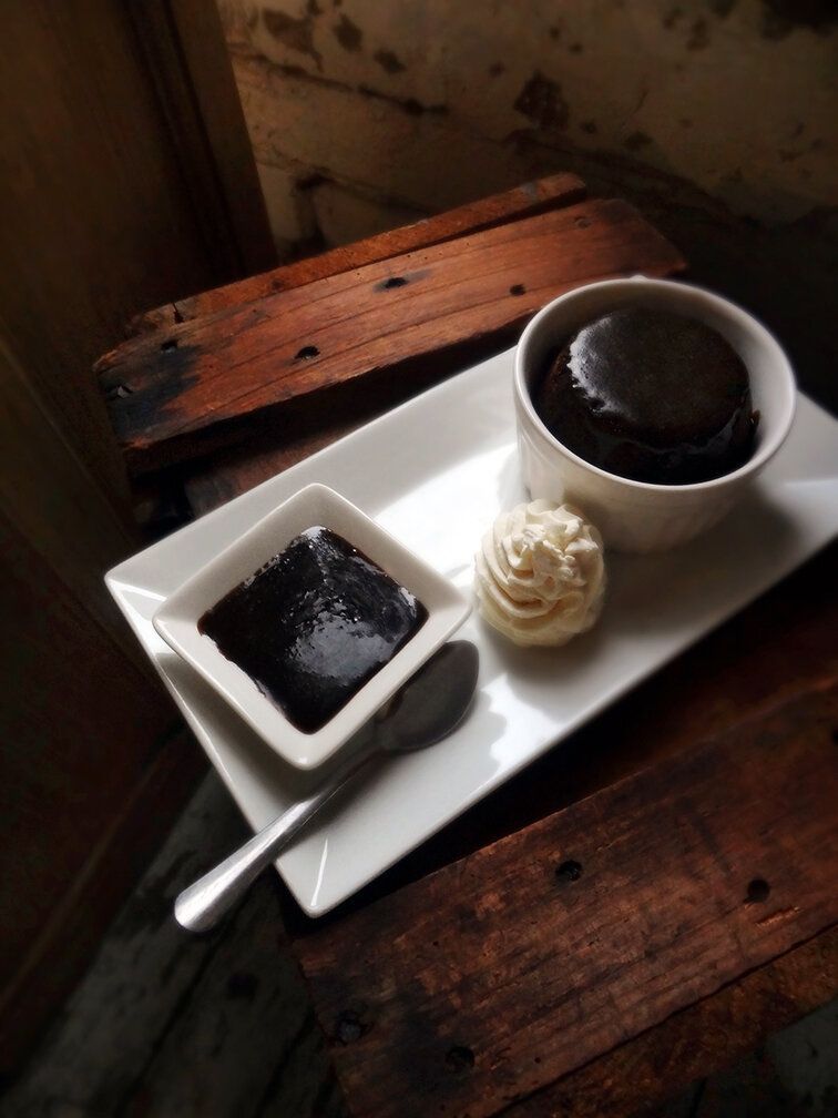 A chocolate lava cake, a side of sauce, and whipped cream on a white tray set on a rustic wooden surface.
