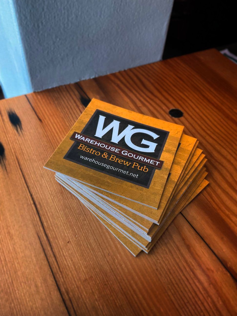 A stack of yellow Warehouse Gourmet BBQ and Brew Pub coasters sitting on a wooden table.
