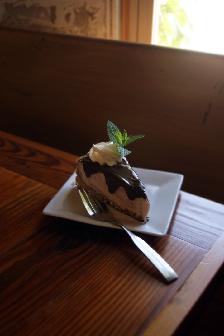 A slice of chocolate pie topped with whipped cream and a mint sprig on a white plate with a fork on a wooden table.