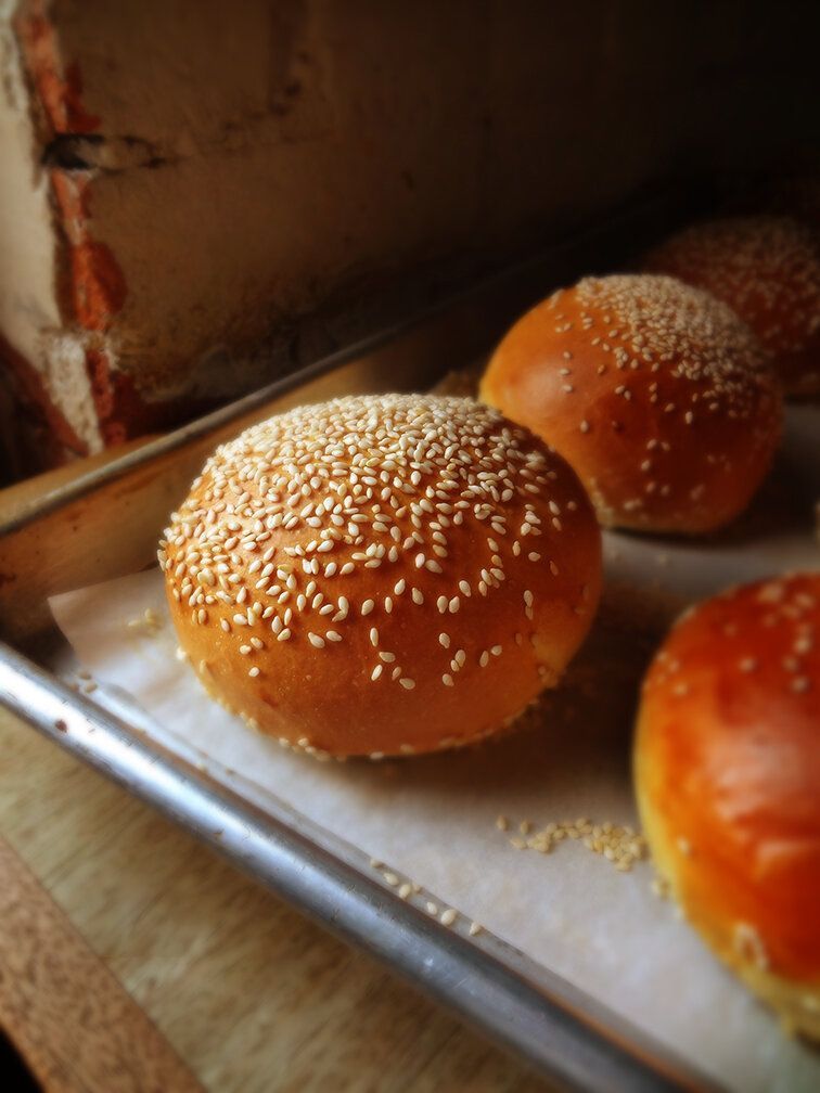 Freshly baked sesame seed buns arranged on a parchment-lined metal baking tray.