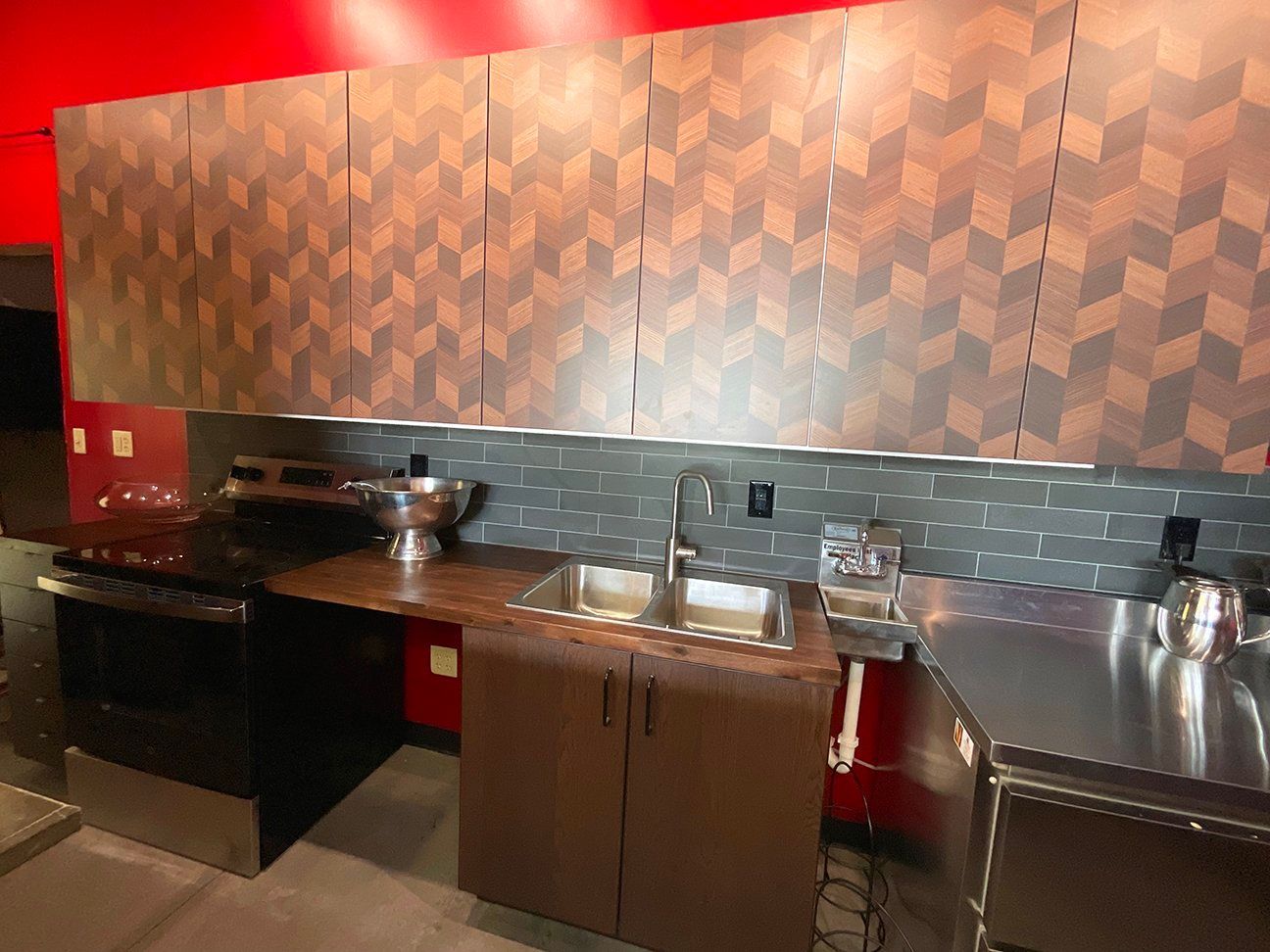 A kitchen area featuring upper cabinets with a geometric wood pattern, dark tile backsplash, a sink, and stainless steel.
