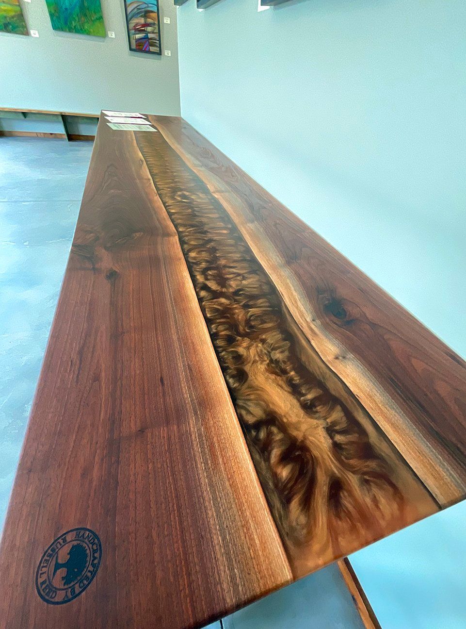 A wooden console table with a textured, live-edge resin inlay running down the center, featuring a circular logo.