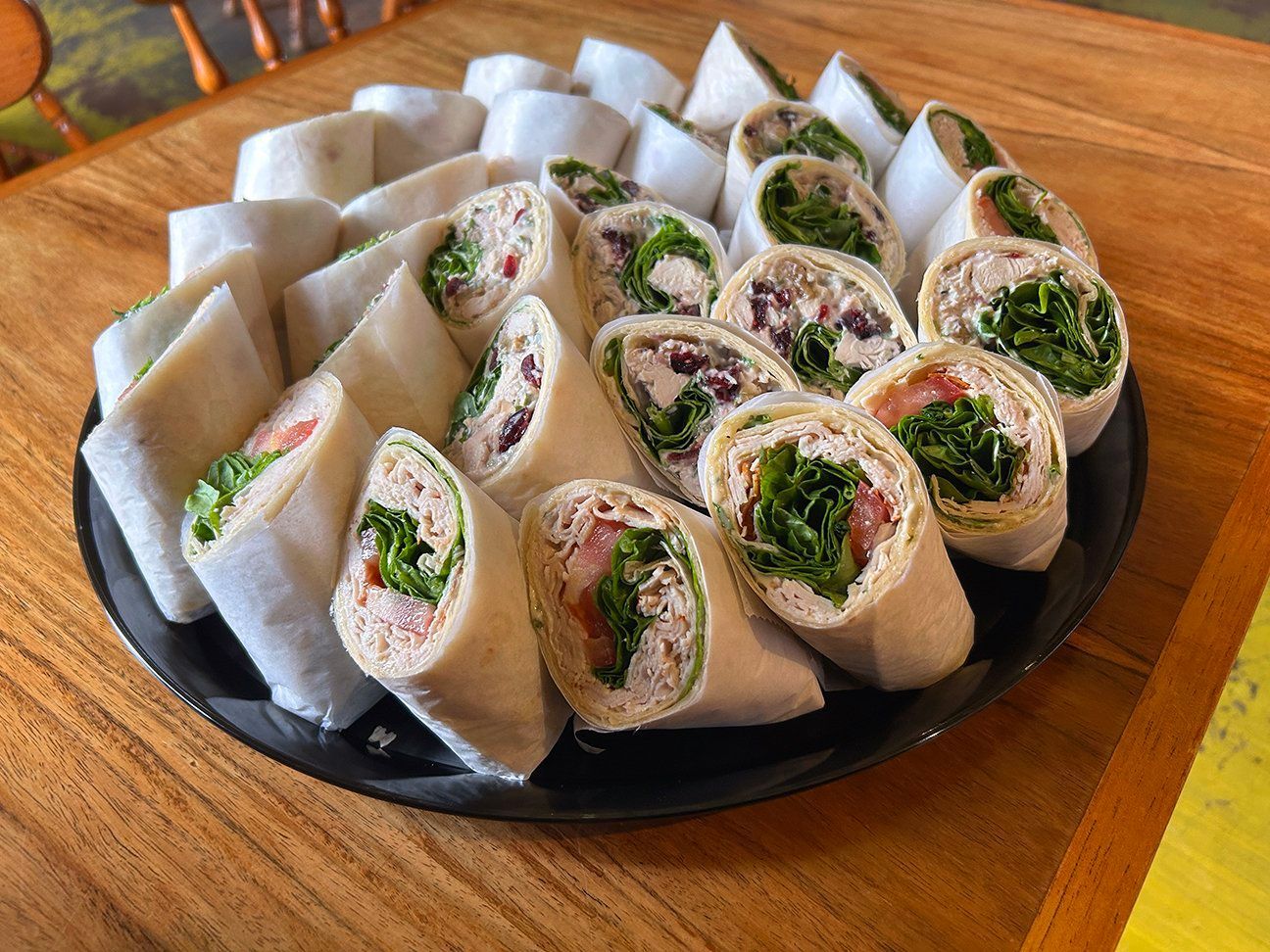 A black platter filled with sliced turkey, cranberry, and lettuce wraps on a wooden table.