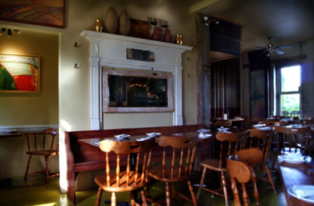 Interior view of a cozy, rustic restaurant with wooden chairs, a long booth, and a decorative fireplace mantel.