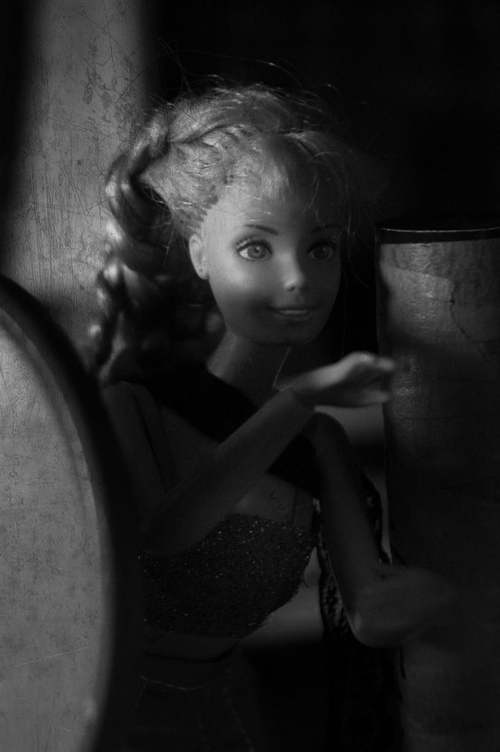 A high-contrast black-and-white close-up of a doll with curly hair, partially obscured by shadow, looking toward the right.
