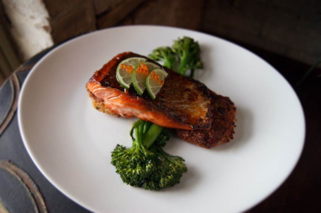 A pan-seared salmon fillet topped with lime slices on a white plate, garnished with steamed broccoli florets.