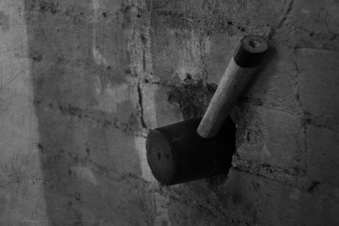 A close-up, black-and-white view of a dark, cylindrical electrical switch mounted on a textured, weathered brick wall.