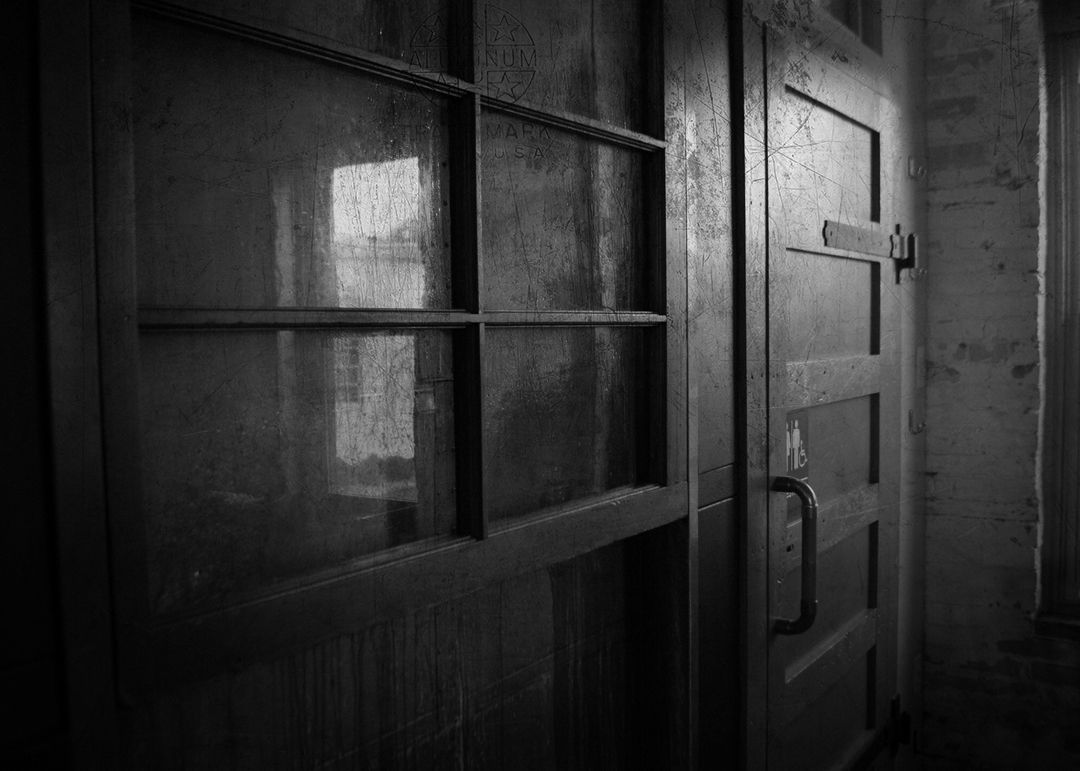 A dimly lit interior view of a glass-paned door adjacent to a wooden paneled door with a handle, showing textured surfaces.