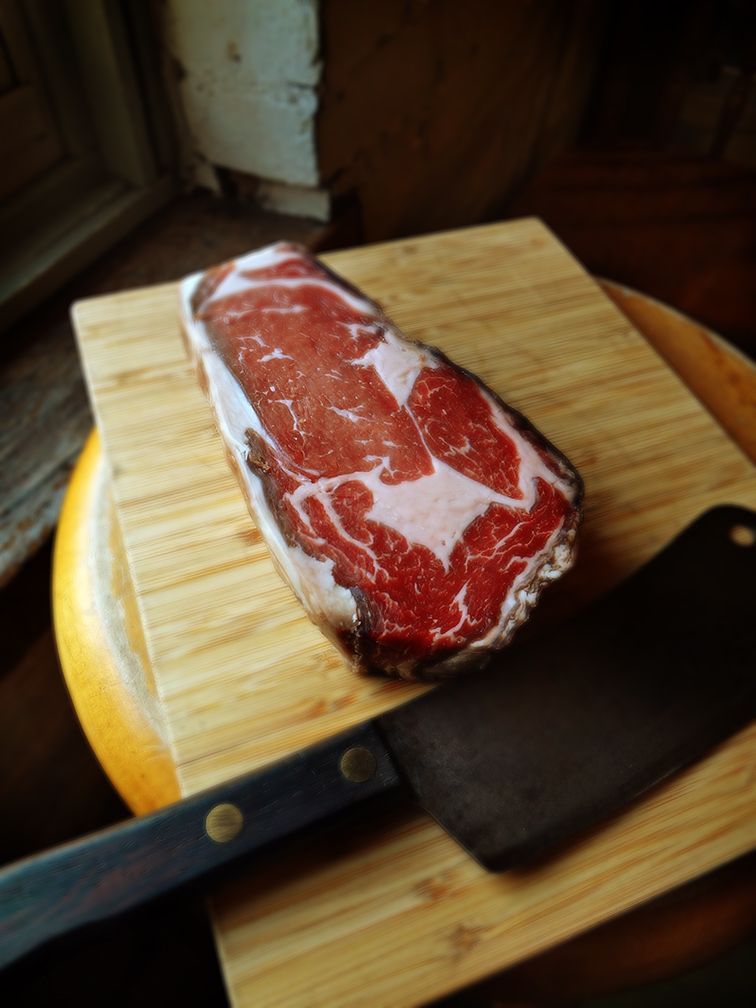 A raw, marbled beef steak on a wooden cutting board next to a meat cleaver.